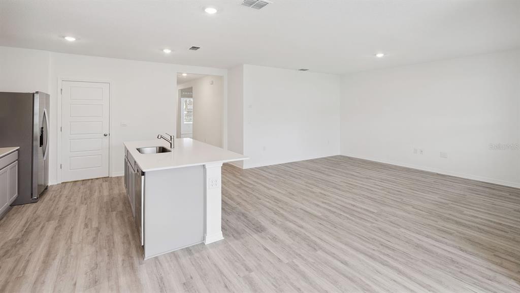 A kitchen with a white island and stainless steel refrigerator opens into a large living area — 7876 FORREST FOX WAY, LAKELAND, FL