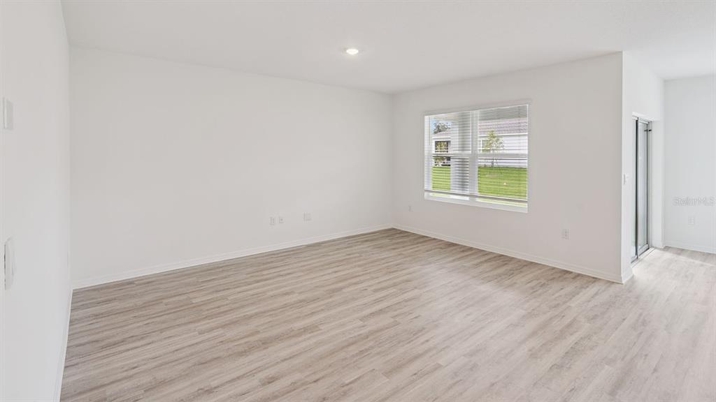 An empty room with light wood-look flooring, white walls, a window, and sliding glass doors — 7876 FORREST FOX WAY, LAKELAND, FL