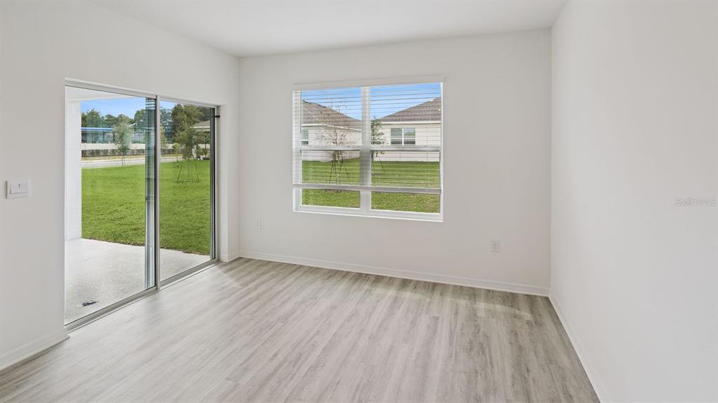 An empty room with light wood-look flooring, a large window, and a sliding glass door — 7876 FORREST FOX WAY, LAKELAND, FL