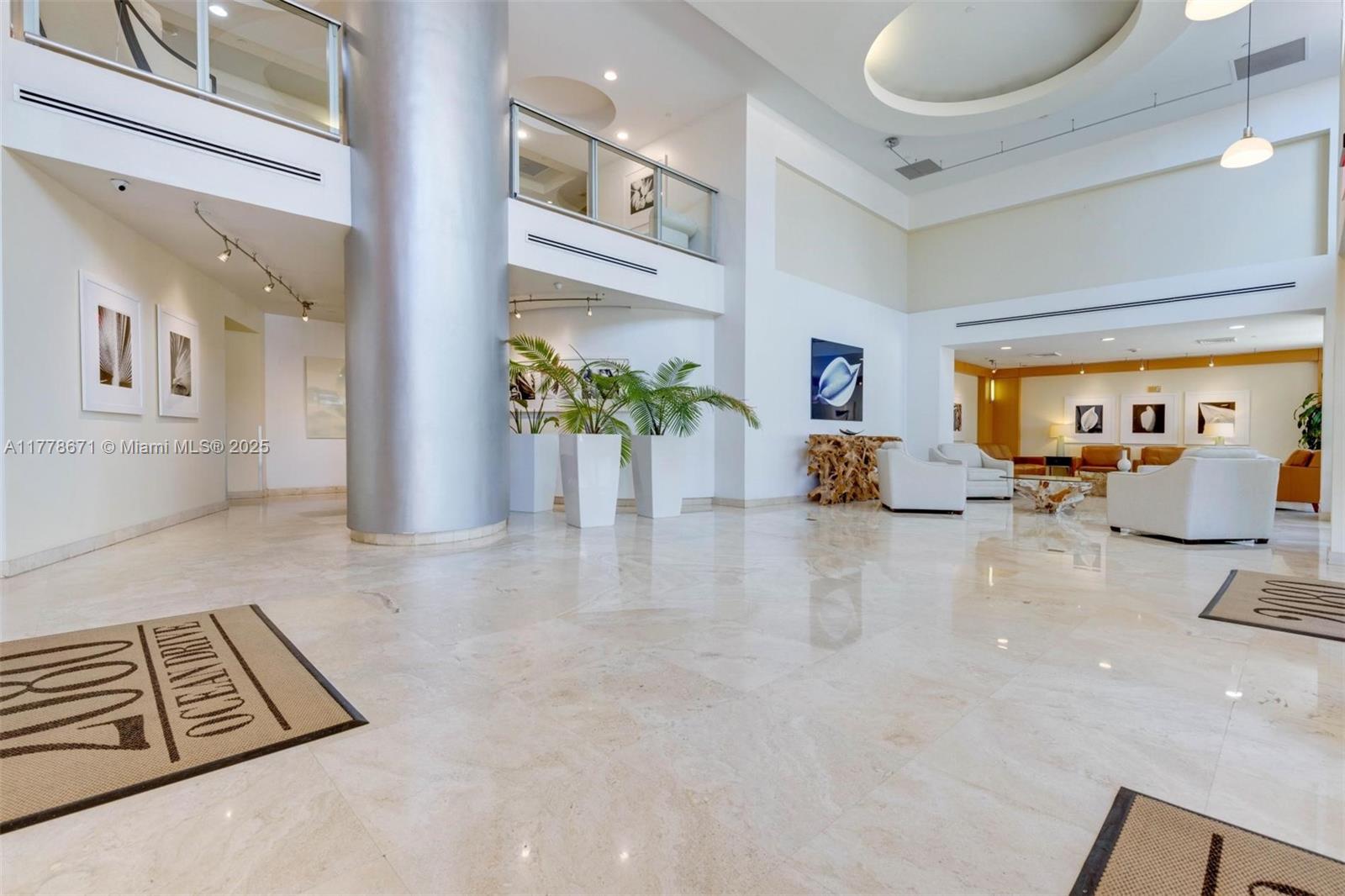 A spacious, modern lobby features polished marble floors, a large silver column, and white furniture — 2080 S Ocean Dr, Hallandale Beach FL 33009, HALLANDALE BEACH, FL