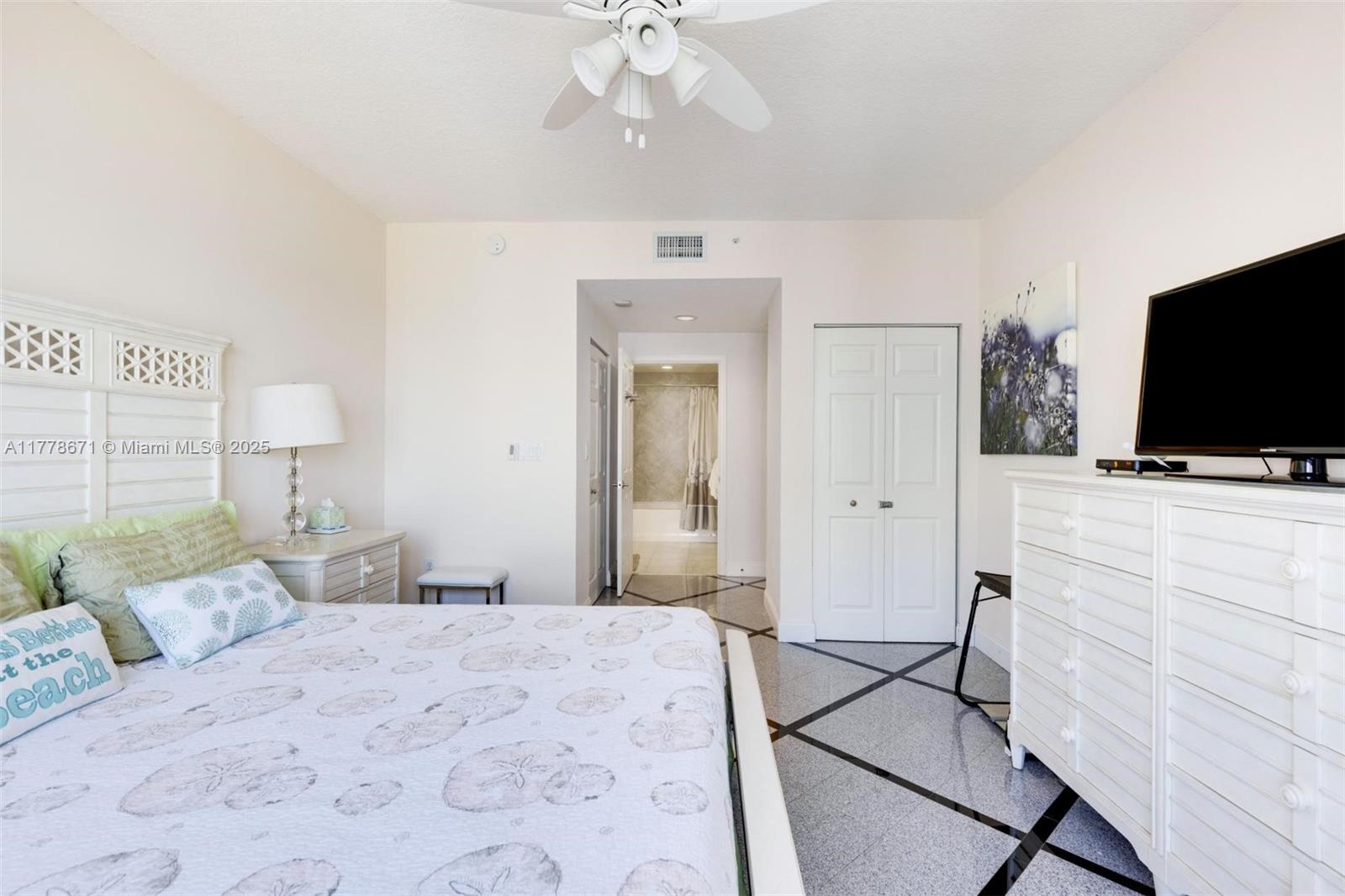 A bedroom features a white bed, a dresser with a television, and tiled flooring — 2080 S Ocean Dr, Hallandale Beach FL 33009, HALLANDALE BEACH, FL