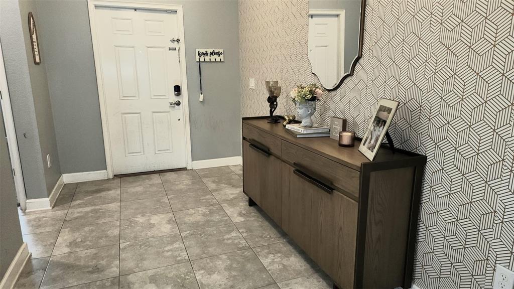An entryway features gray tile flooring, a white front door, and a geometric patterned accent wall — 4687 FAIRY TALE CIRCLE, KISSIMMEE, FL