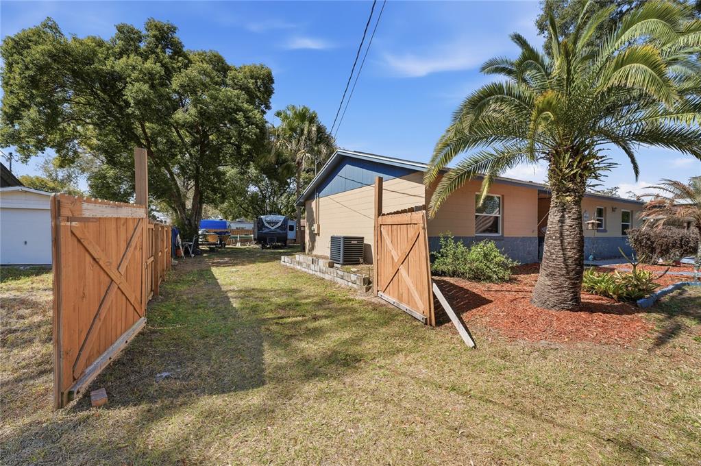 A side view of a house exterior featuring a wooden fence and a palm tree — 2670 REAGAN LANE, KISSIMMEE, FL