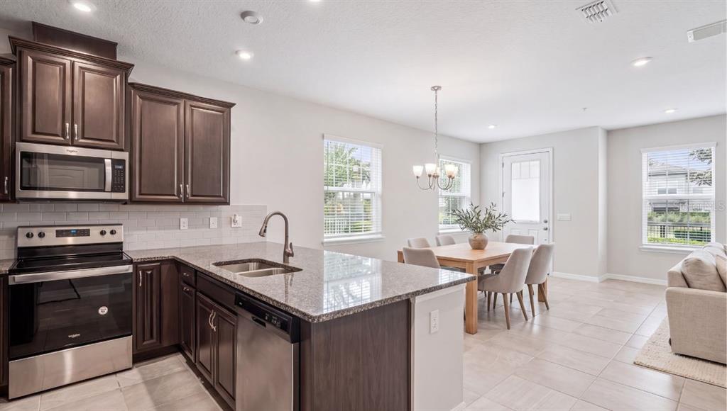 A kitchen with dark wood cabinets, granite countertops, and stainless steel appliances opens to dining — 9457 RANDAL PARK BOULEVARD, ORLANDO, FL