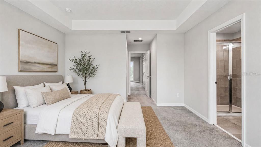 A bedroom with a tray ceiling, gray carpet, and an attached bathroom with a shower — 9457 RANDAL PARK BOULEVARD, ORLANDO, FL