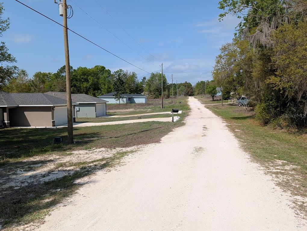 A gravel road leads past a modern house with a garage toward a wooded area — SW 30TH PLACE, OCALA, FL