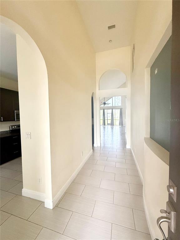 A tiled entryway leads through an arched hallway toward a bright living area with large windows — 4349 CRYSTAL DOWNS COURT, WESLEY CHAPEL, FL