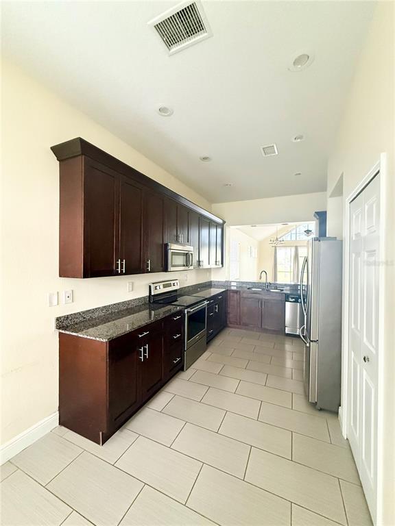 A kitchen features dark wood cabinets, granite countertops, stainless steel appliances, and light tile flooring — 4349 CRYSTAL DOWNS COURT, WESLEY CHAPEL, FL