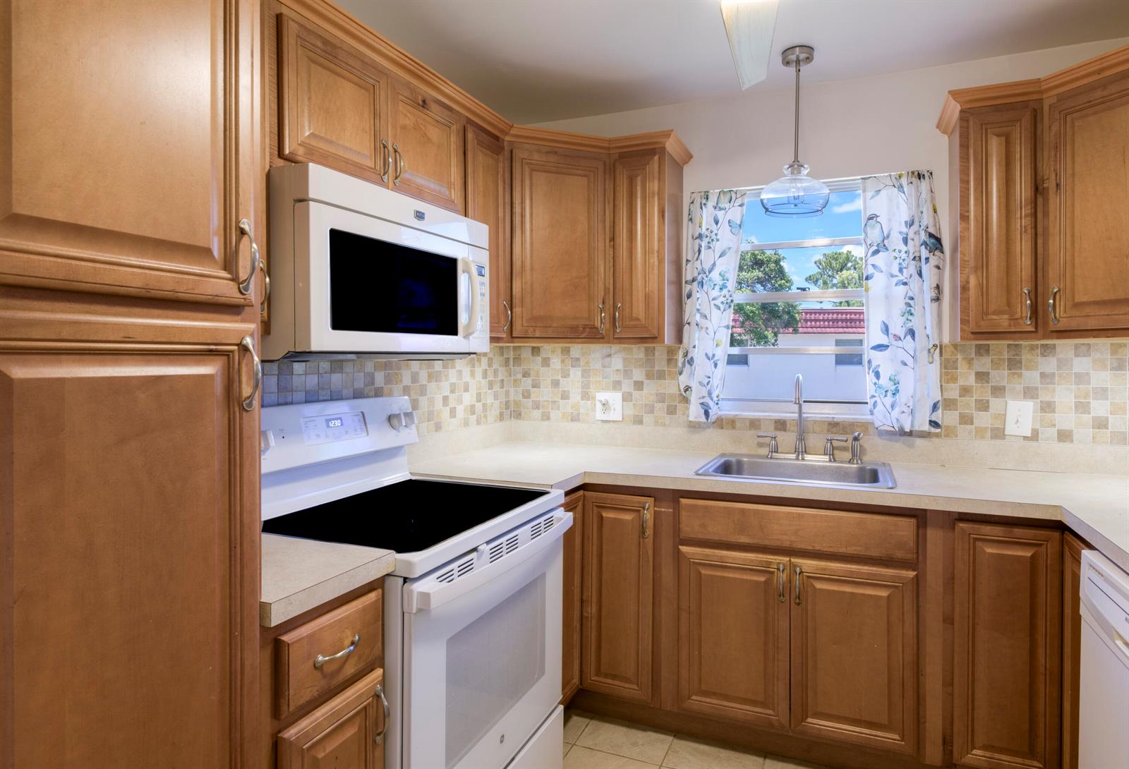 A kitchen features wood cabinets, white appliances, a tiled backsplash, and a window over the sink — 1225 NW 21st Street # 1615, Stuart FL 34994, STUART, FL