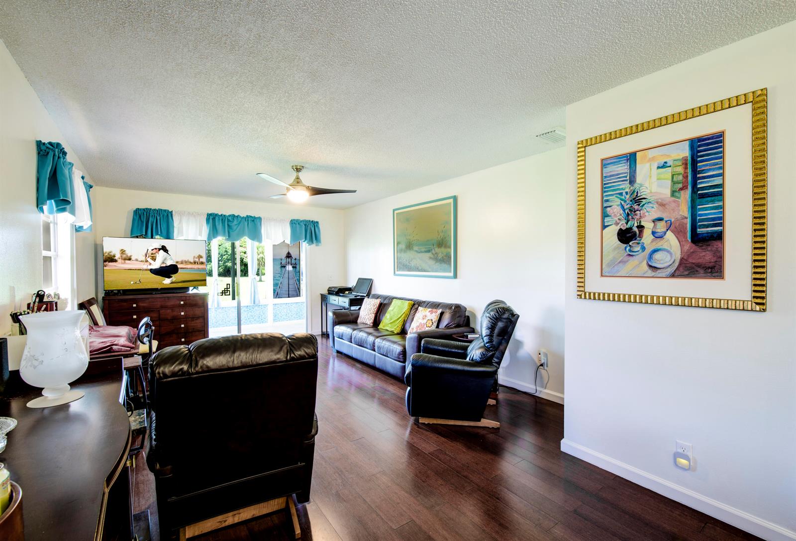 A living room features dark wood flooring, a leather sofa, and a large framed painting — 1225 NW 21st Street # 1615, Stuart FL 34994, STUART, FL