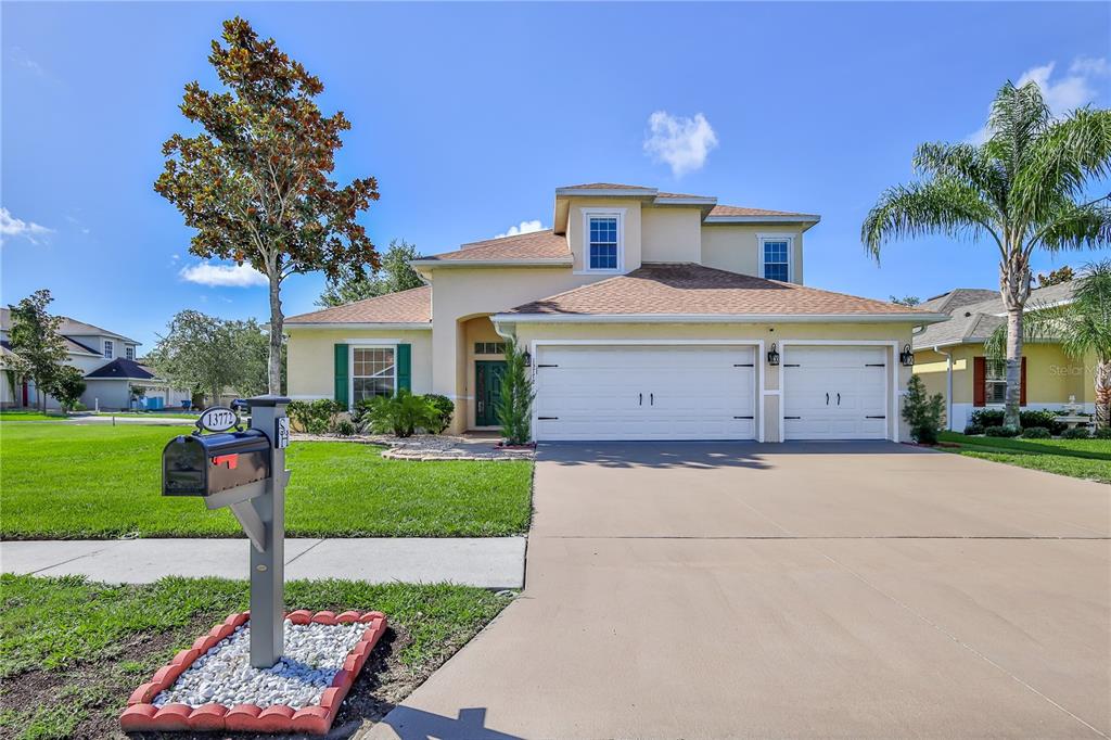A two-story suburban house with a tan stucco exterior, a three-car garage, and a lawn — 13772 DUNWOODY DRIVE, SPRING HILL, FL