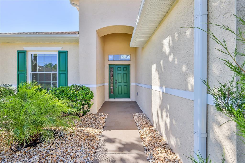 A beige stucco house exterior features a green front door and green window shutters — 13772 DUNWOODY DRIVE, SPRING HILL, FL