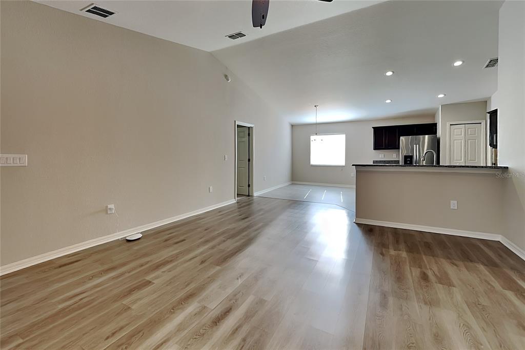 An open-concept living area with light wood-look flooring leads to a kitchen with dark cabinets — 505 INTERLOCK STREET, LAKE ALFRED, FL