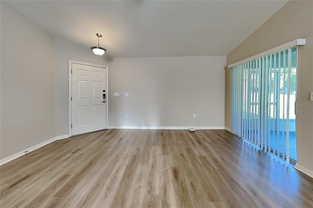 An empty living room features light wood-look flooring, a white front door, and vertical blinds — 505 INTERLOCK STREET, LAKE ALFRED, FL