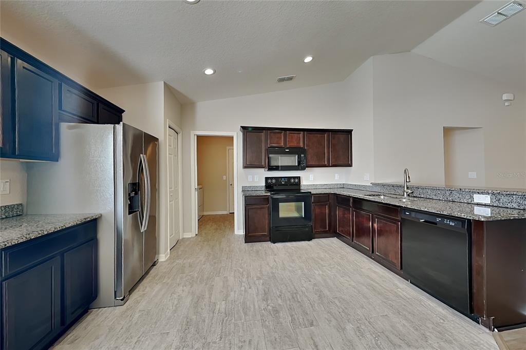 A kitchen features dark wood cabinets, granite countertops, stainless steel appliances, and light wood-look flooring — 505 INTERLOCK STREET, LAKE ALFRED, FL
