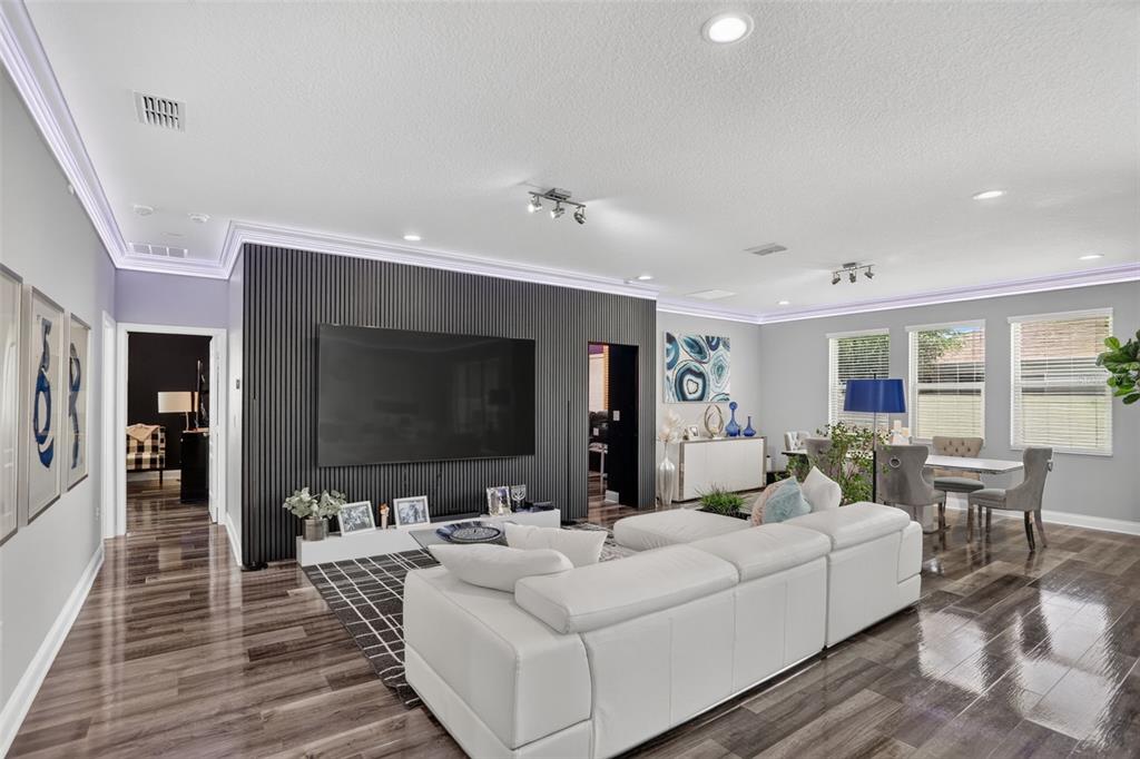 A modern living room features a slatted black accent wall, white sectional sofa, and hardwood floors — 5352 COSTA DEL SOL DRIVE, ST CLOUD, FL