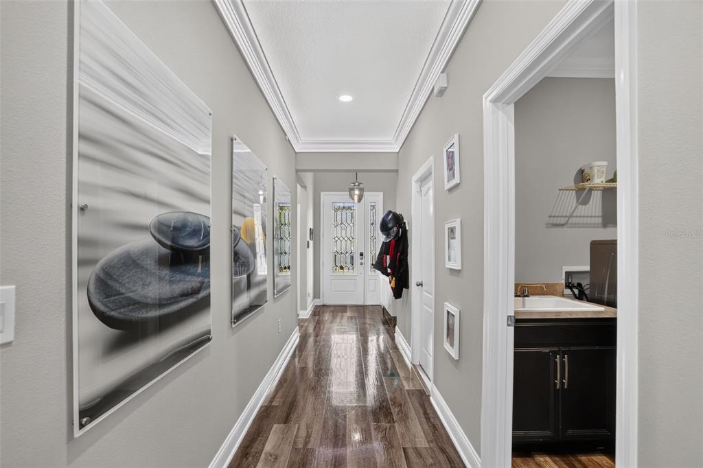 A hallway with wood-look flooring leads to a front door, featuring wall art and a laundry room — 5352 COSTA DEL SOL DRIVE, ST CLOUD, FL