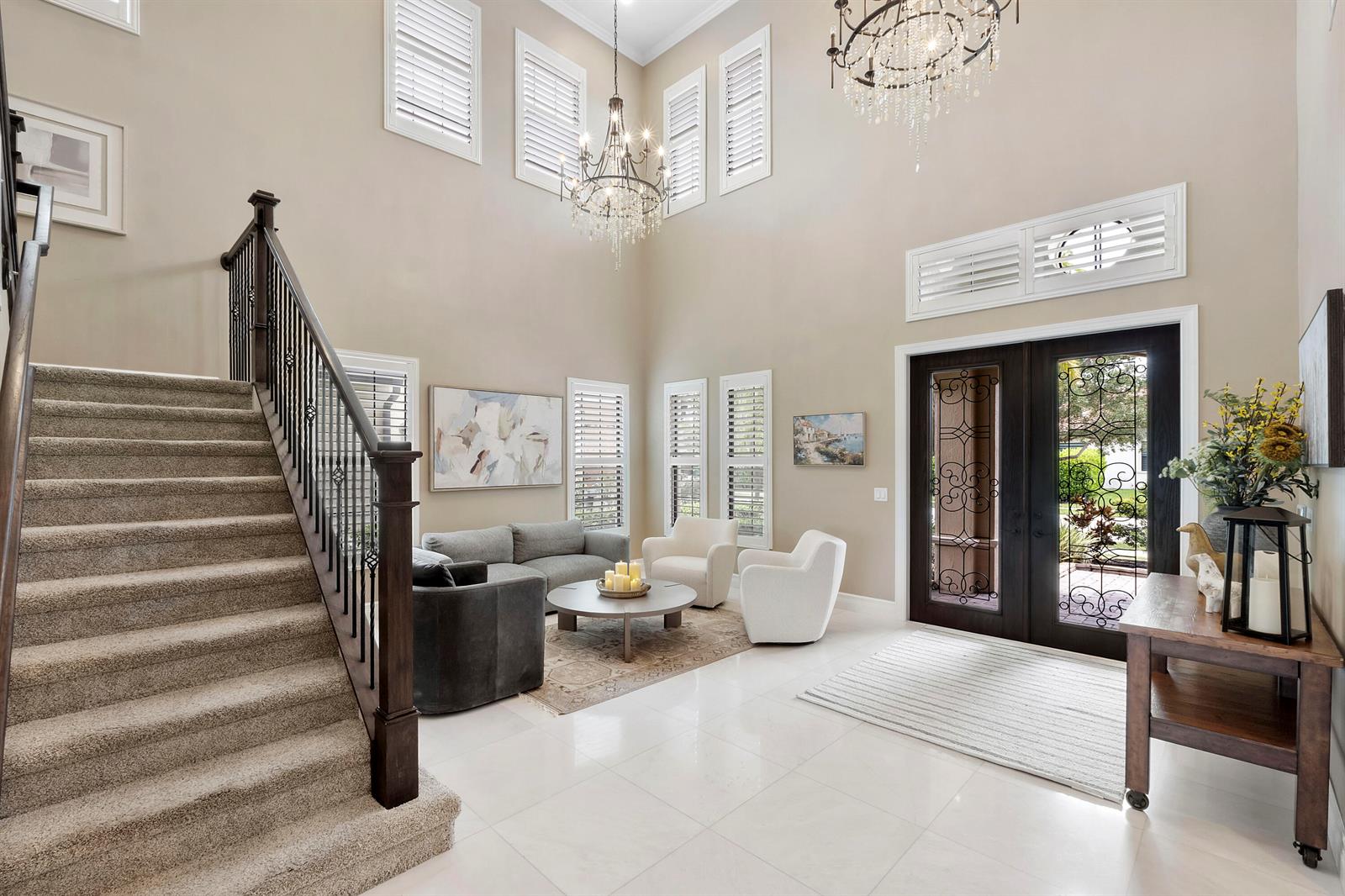 A high-ceilinged foyer features a carpeted staircase, tile flooring, two chandeliers, and a seating area — 11525 NW 81st Place, Parkland FL 33076, PARKLAND, FL