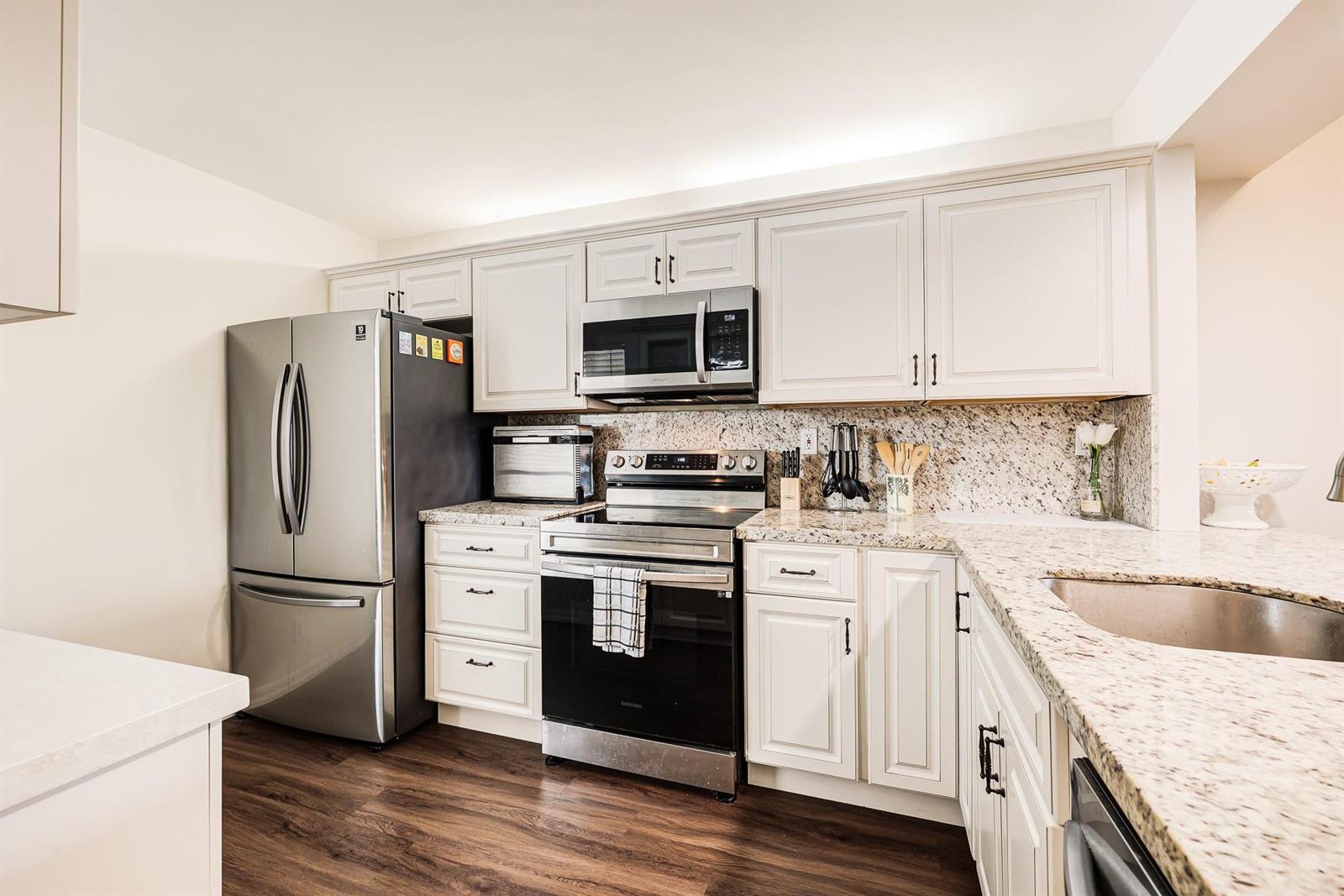 A kitchen features white cabinets, granite countertops, stainless steel appliances, and dark wood flooring — 6 Royal Palm Way # 303, Boca Raton FL 33432, BOCA RATON, FL