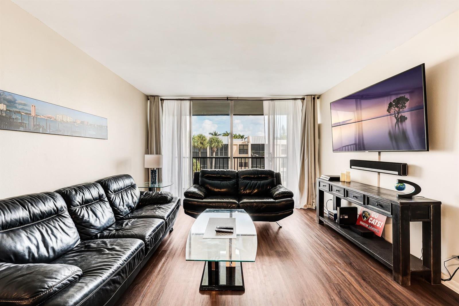 A living room features black leather sofas, a glass coffee table, and a wall-mounted television — 6 Royal Palm Way # 303, Boca Raton FL 33432, BOCA RATON, FL