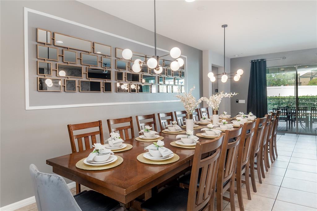 A long wooden dining table is set for many guests beneath two modern globe chandeliers — 2137 MALTA TERRACE, KISSIMMEE, FL