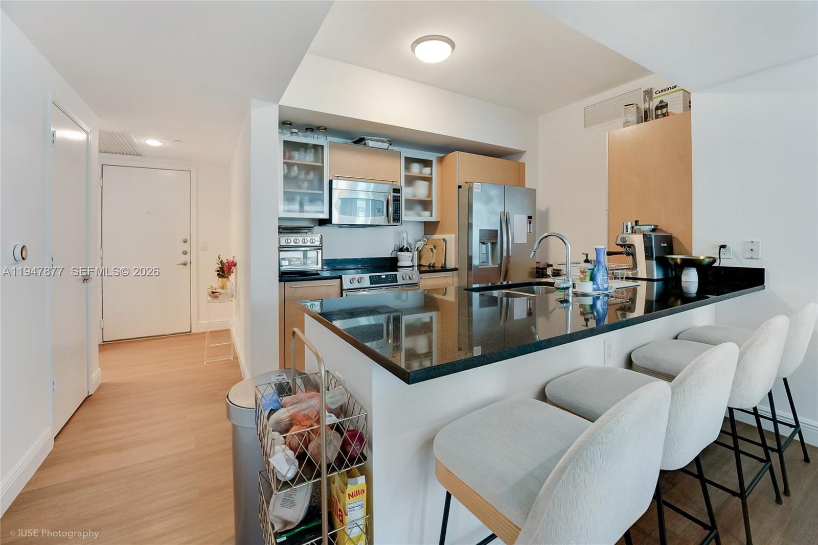 A modern kitchen features dark granite countertops, stainless steel appliances, and a breakfast bar with stools — 951 Brickell Ave # 1110, Miami FL 33131, MIAMI, FL