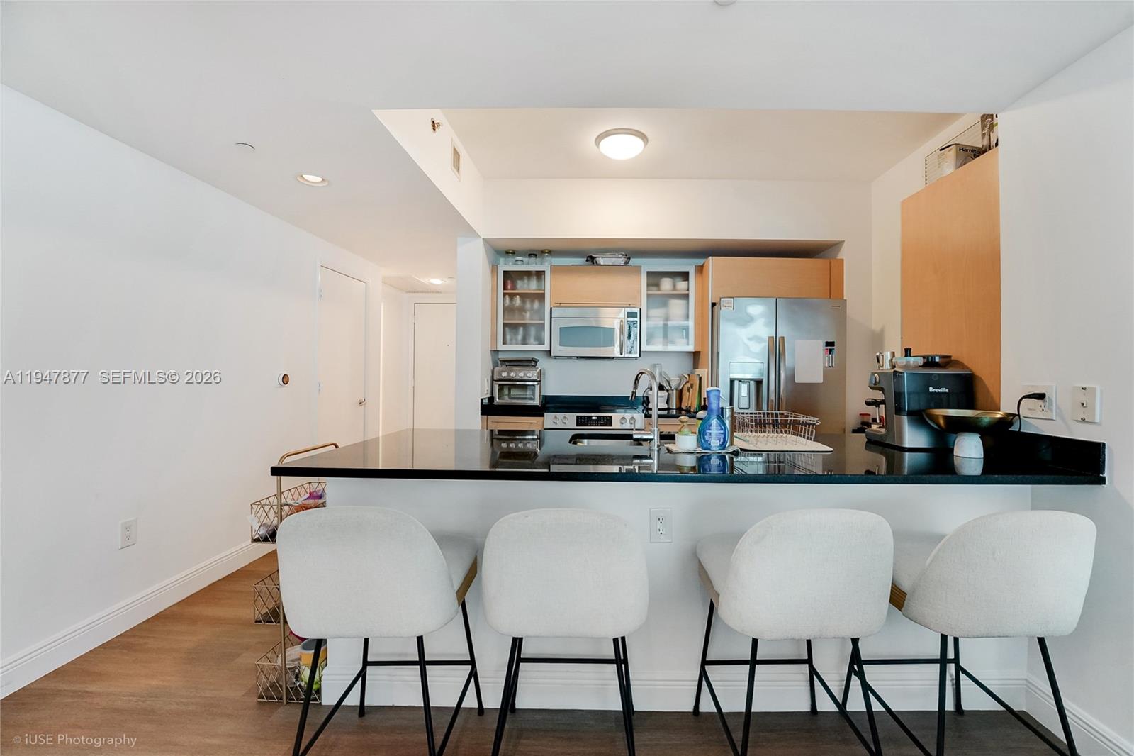 A kitchen features a black countertop island, white bar stools, and stainless steel appliances — 951 Brickell Ave # 1110, Miami FL 33131, MIAMI, FL