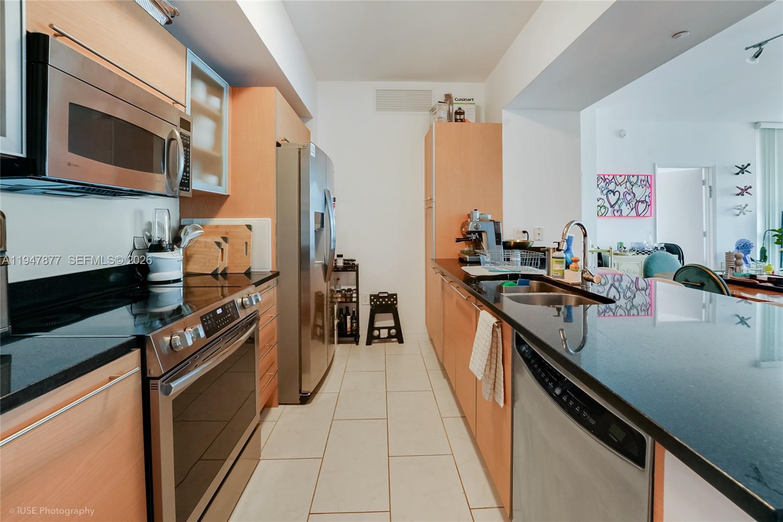 A galley kitchen features light wood cabinets, black countertops, and stainless steel appliances — 951 Brickell Ave # 1110, Miami FL 33131, MIAMI, FL