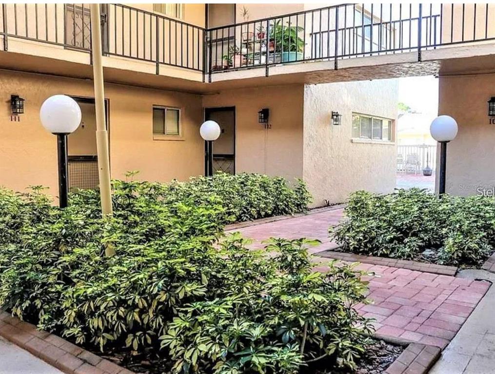 A courtyard with brick walkways, lush green shrubs, and apartment entrances with globe lighting — 2763 WOODGATE LANE UNIT 211, SARASOTA, FL