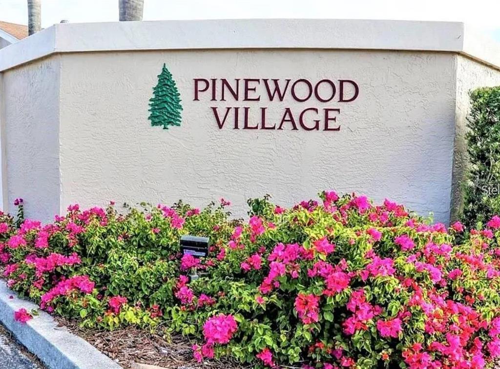 A sign for Pinewood Village sits behind a large bush of bright pink flowers — 2763 WOODGATE LANE UNIT 211, SARASOTA, FL