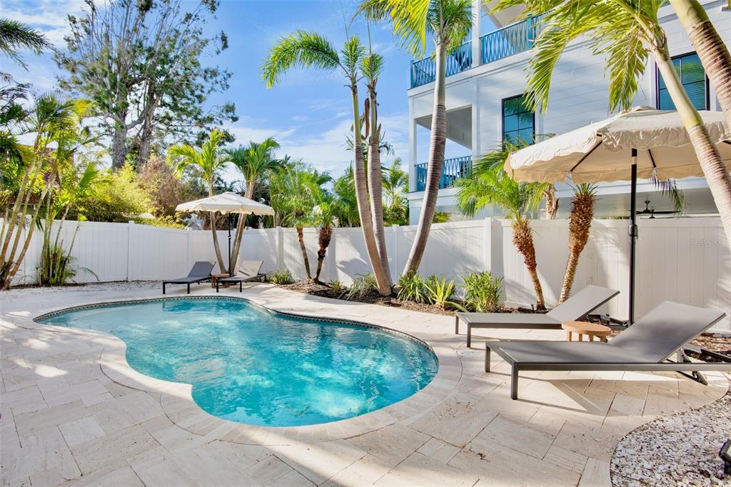 A backyard swimming pool with lounge chairs, umbrellas, and palm trees surrounded by a white fence — 709 FERN STREET, ANNA MARIA, FL