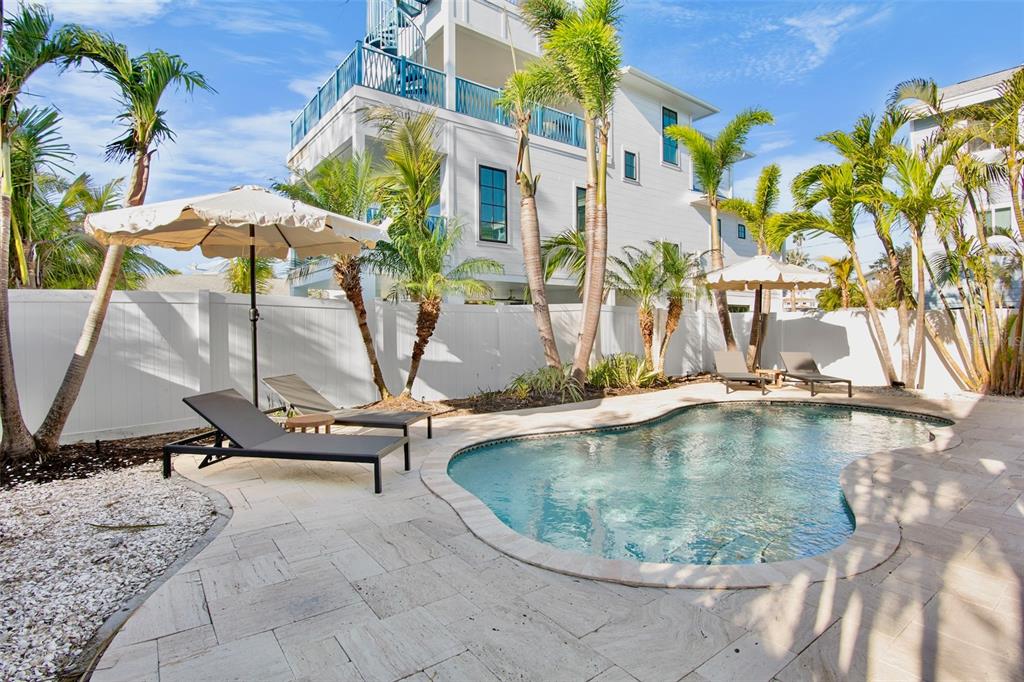 A swimming pool with lounge chairs and umbrellas sits in a backyard with palm trees — 709 FERN STREET, ANNA MARIA, FL