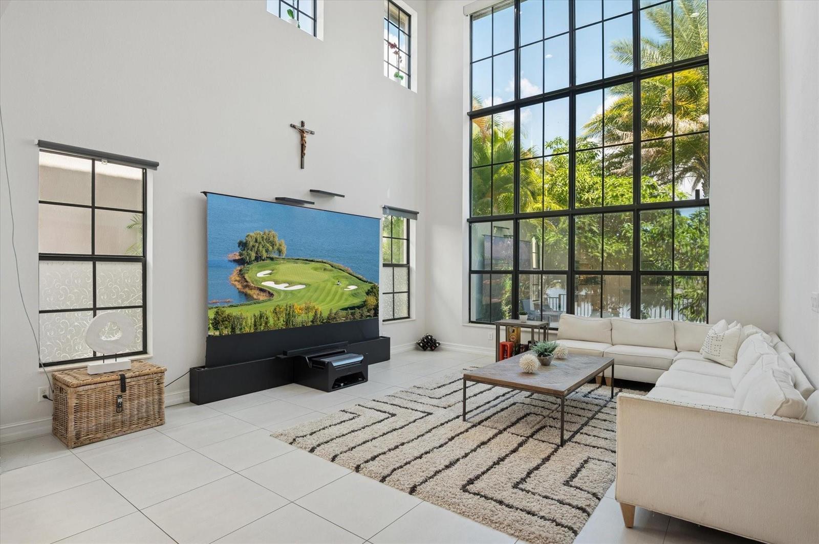 A bright living room features a large projection screen, floor-to-ceiling windows, and white tile flooring — 11515 Horizon Road, Parkland FL 33076, PARKLAND, FL