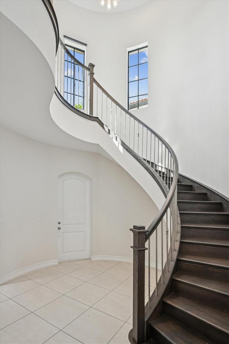 A curved wooden staircase with metal railings stands in a bright, tiled entryway — 11515 Horizon Road, Parkland FL 33076, PARKLAND, FL