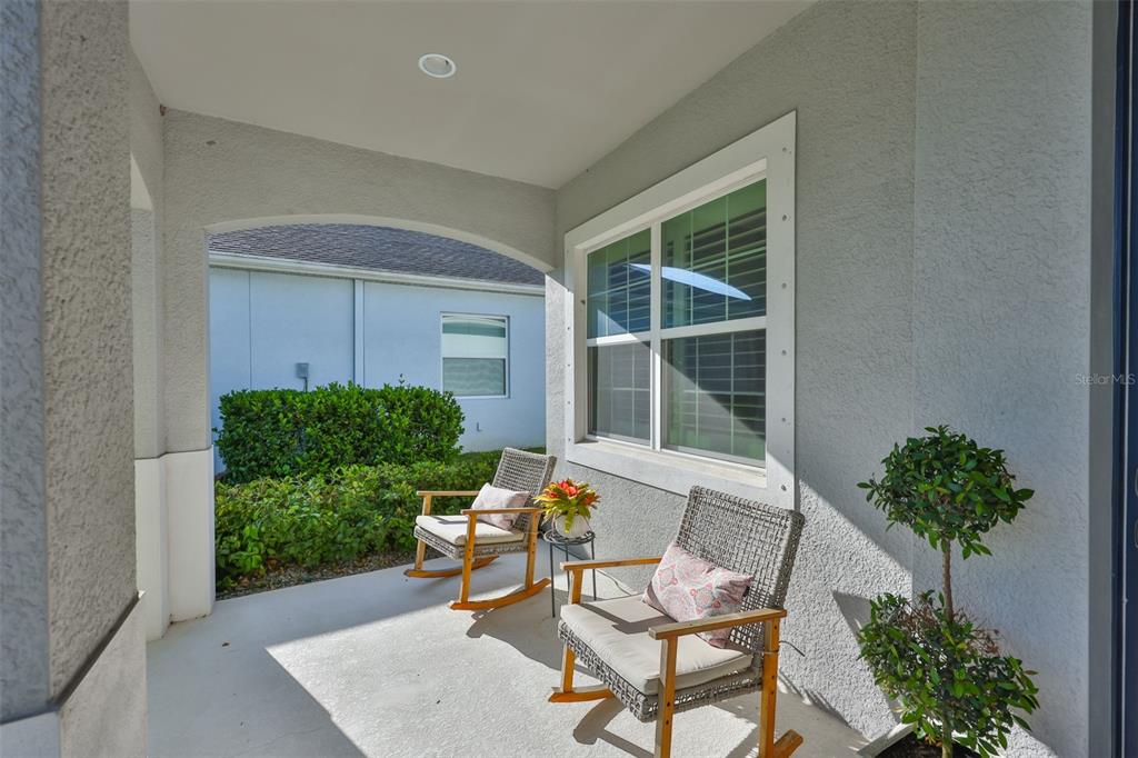 A covered concrete porch features two rocking chairs and a small potted plant — 12421 GLENRIDGE LANE, PARRISH, FL