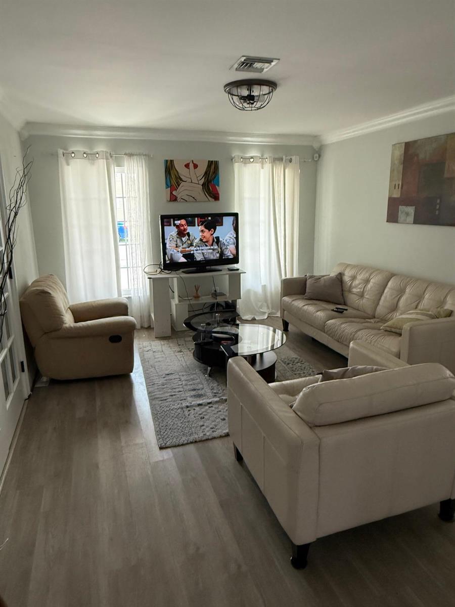 A living room with light wood flooring, beige furniture, a television, and white curtains — 3400 Ivy Way, Miramar FL 33025, MIRAMAR, FL