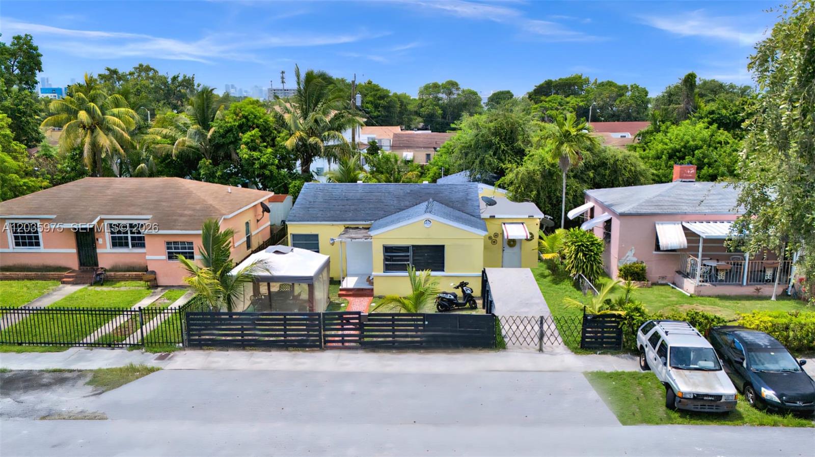 An exterior view of three single-story houses with fenced yards and parked vehicles — 1042 NW 76th St, Miami FL 33150, MIAMI, FL