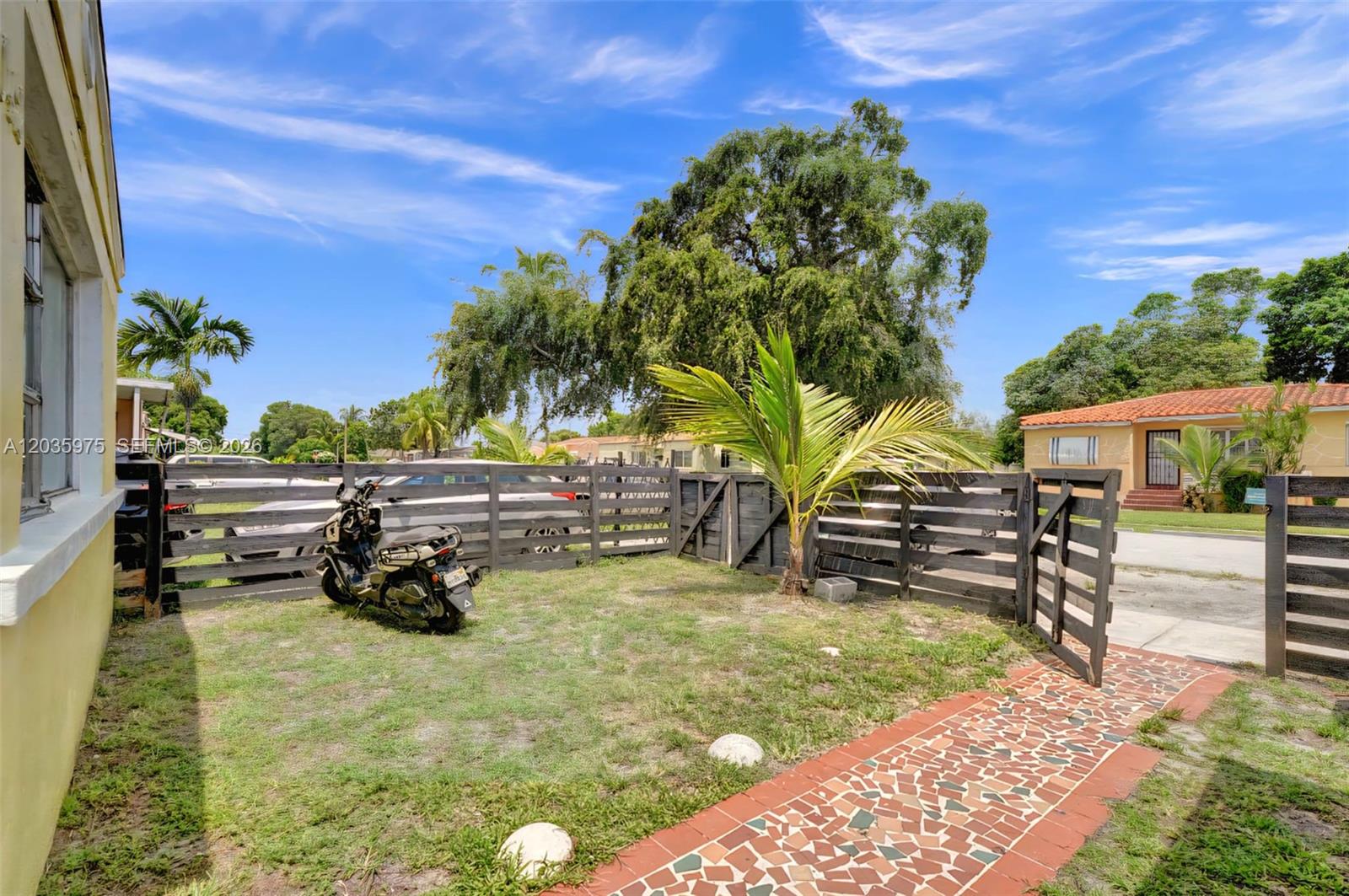 A small yard features a motorcycle, a wooden fence, and a mosaic-tiled walkway — 1042 NW 76th St, Miami FL 33150, MIAMI, FL