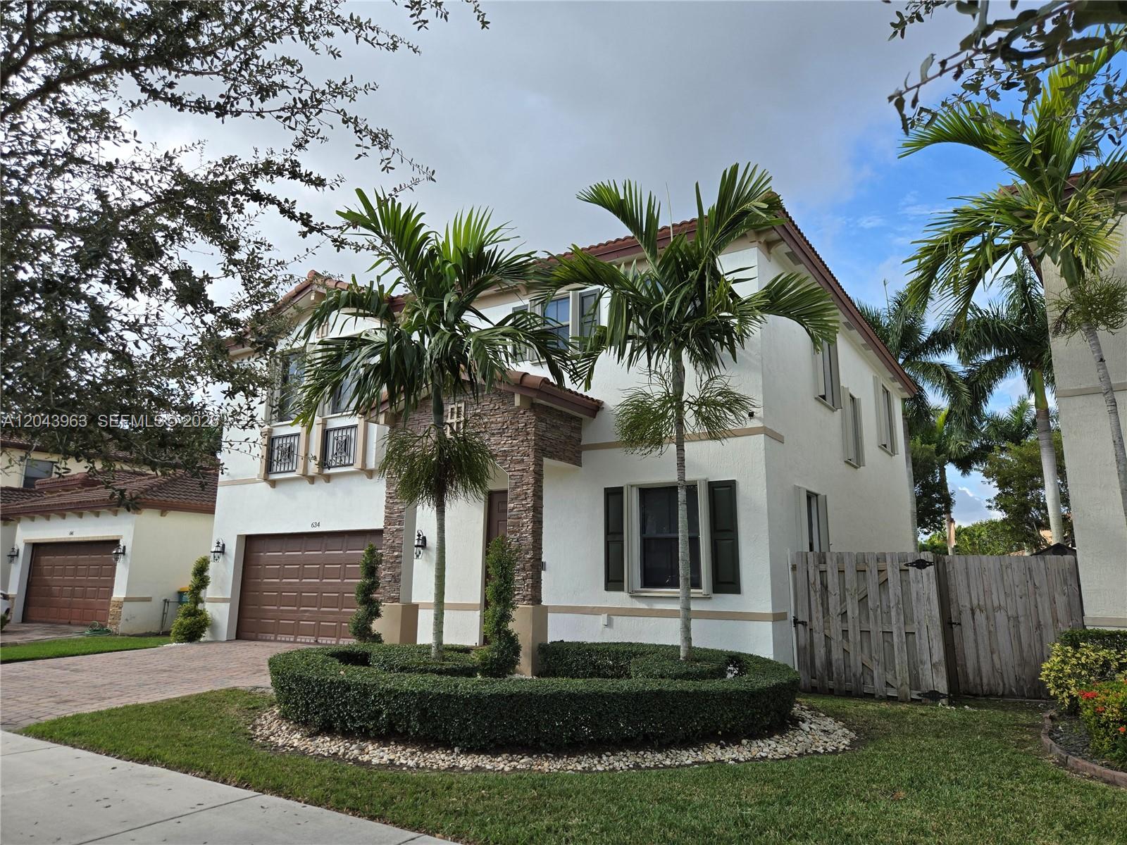 A two-story stucco house features a stone-accented entryway, palm trees, and a manicured hedge — 634 SE 37 Ave, Homestead FL 33033, HOMESTEAD, FL