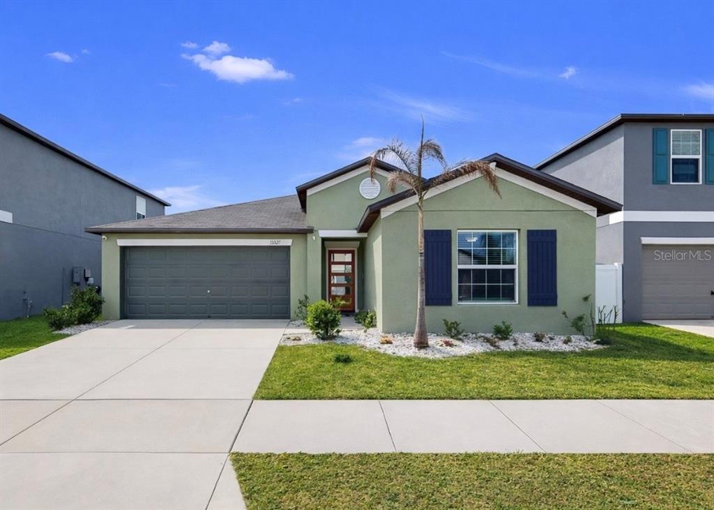 A single-story house with green stucco siding, a two-car garage, and blue shutters — 13327 GREAT PLAINS DRIVE, RIVERVIEW, FL