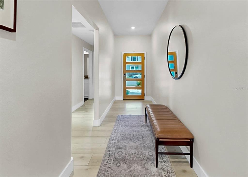A hallway features light wood flooring, a patterned runner rug, a leather bench, and a mirror — 13327 GREAT PLAINS DRIVE, RIVERVIEW, FL