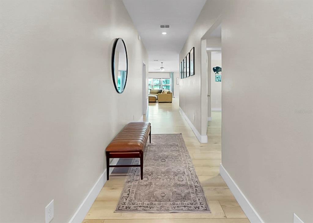 A long hallway features light wood flooring, a brown leather bench, and a patterned rug — 13327 GREAT PLAINS DRIVE, RIVERVIEW, FL