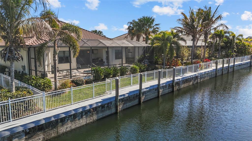A waterfront house features a screened-in patio, a white fence, and several palm trees — 576 MAST DRIVE, BRADENTON, FL