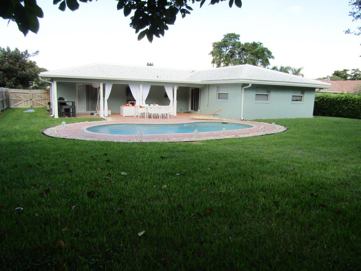 A backyard view of a single-story house with a white roof, patio, and swimming pool — 3244 NW 25th Way, Boca Raton FL 33434, BOCA RATON, FL