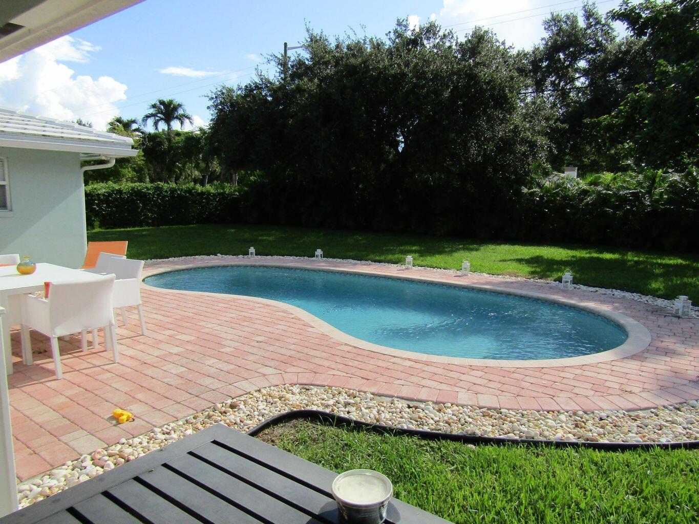 A kidney-shaped swimming pool sits in a backyard with a red brick patio and lawn — 3244 NW 25th Way, Boca Raton FL 33434, BOCA RATON, FL