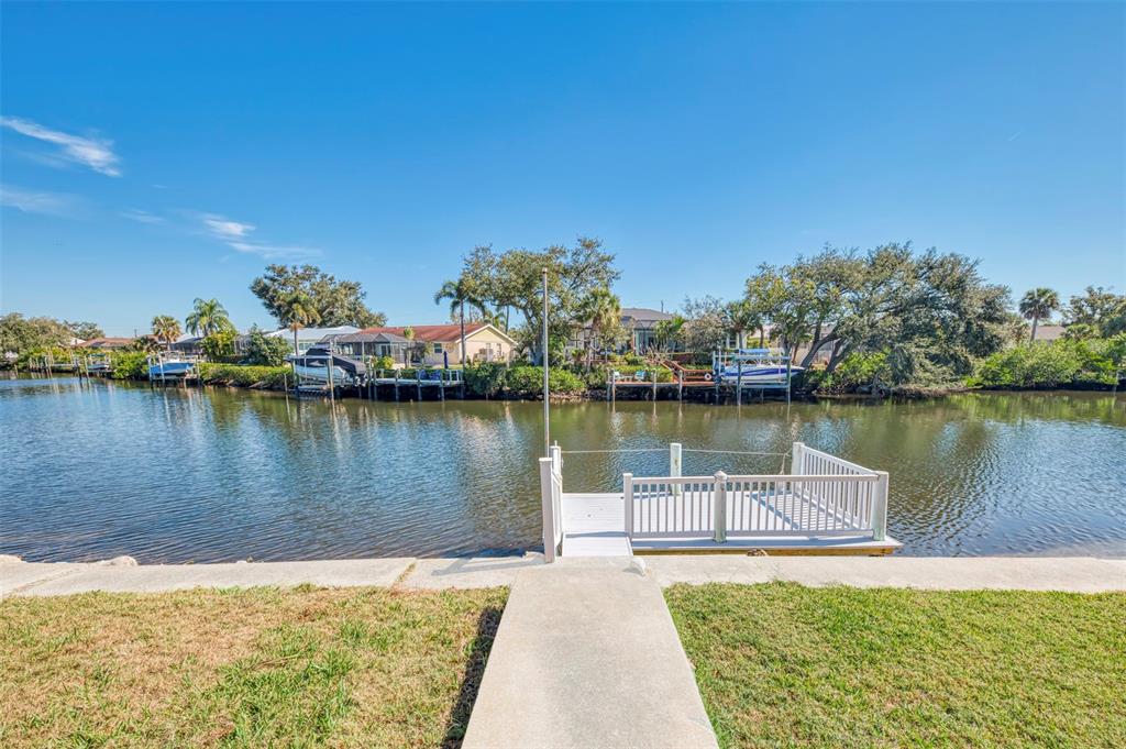 A concrete walkway leads to a white wooden dock overlooking a canal with boats — 602 PORTIA STREET N, NOKOMIS, FL