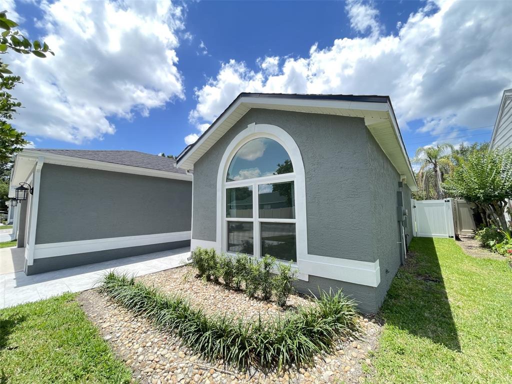A gray stucco house exterior features a large arched window and a rock garden — 2869 FALLING TREE CIRCLE, ORLANDO, FL