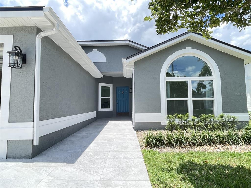 A gray house exterior features a blue front door, arched window, and tiled walkway — 2869 FALLING TREE CIRCLE, ORLANDO, FL