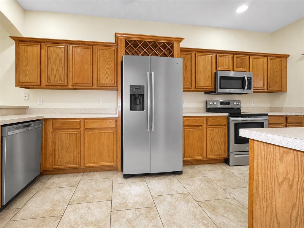 A kitchen features oak cabinets, stainless steel appliances, and light-colored tile flooring — 1602 TAIL FEATHER DRIVE, KISSIMMEE, FL
