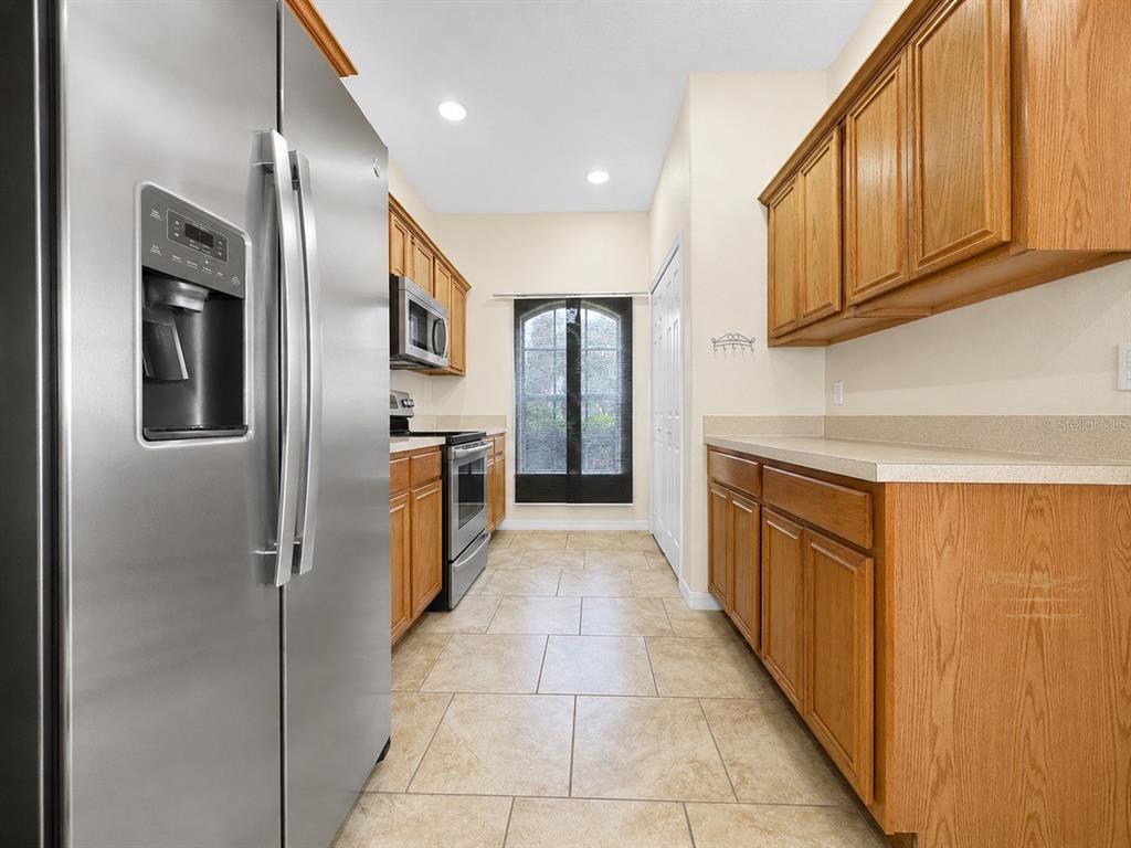 A galley kitchen features stainless steel appliances, oak cabinets, and light-colored tile flooring — 1602 TAIL FEATHER DRIVE, KISSIMMEE, FL